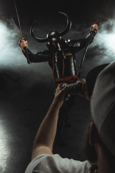 man controlling samurai character with gamepad on black - Foto, imagen