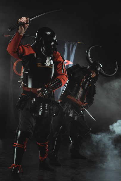 samouraï blindé se battant avec des épées devant les symboles du clan sur les drapeaux sur noir
 - Photo, image