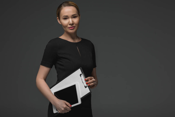 beautiful kazakh businesswoman with digital tablet and clipboard smiling at camera isolated on grey  - Foto, Imagen
