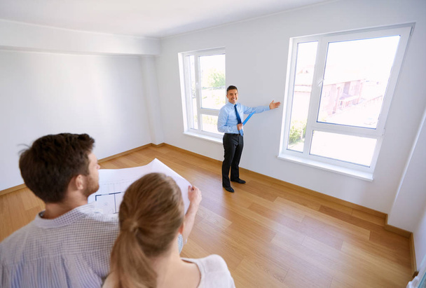 agente inmobiliario mostrando nuevo hogar a pareja con plano
 - Foto, Imagen