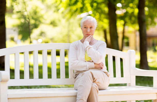 sad senior woman sitting on bench at summer park - Фото, изображение