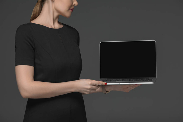 cropped shot of attractive woman holding laptop with blank screen isolated on grey - Fotó, kép