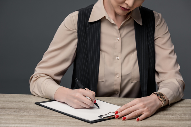 cropped shot of kazakh businesswoman writing on clipboard at table isolated on grey - Fotoğraf, Görsel