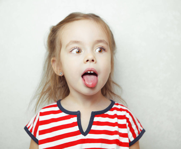 Suloinen pieni tyttö vetää kielensä ulos ja näyttää sivuttain
 - Valokuva, kuva