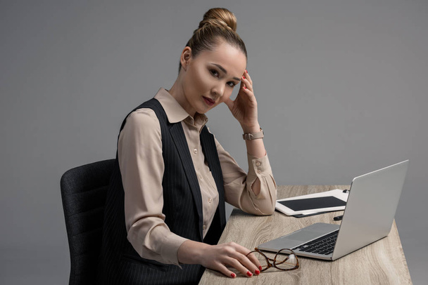 beautiful kazakh businesswoman looking at camera while using laptop isolated on grey  - Фото, зображення