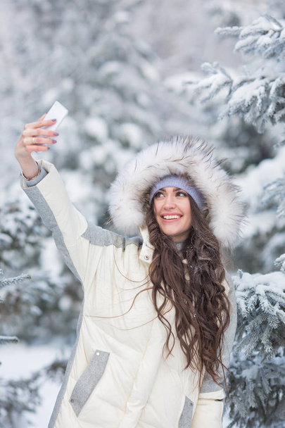 Portrait of smiling young woman does a selfie in the winter forest - Фото, зображення