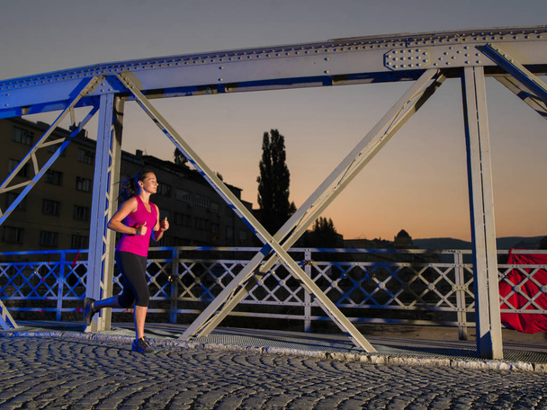 Stadtsport, junge gesunde Frau joggt frühmorgens in der Nacht über die Brücke in der Stadt - Foto, Bild