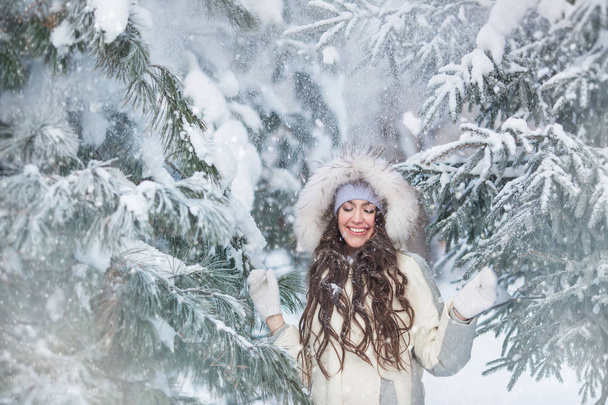 Smiling young woman under a snowfall in the winter forest - Photo, Image
