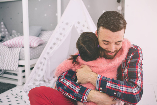 Cute little daughter and her handsome young dad are playing together in childs room. Daddy and child spend time together while sitting on the floor in bedroom. - Φωτογραφία, εικόνα