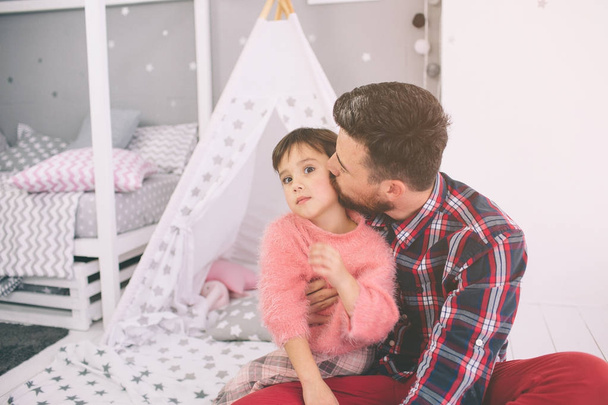 Cute little daughter and her handsome young dad are playing together in childs room. Daddy and child spend time together while sitting on the floor in bedroom. - Фото, изображение
