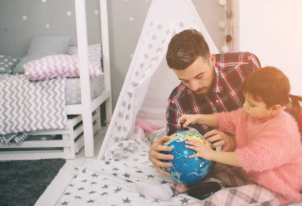 Cute little daughter and her handsome young dad iare playing together in childs room. Happy family of dady and child prepare to travel trip, learn for route map - Φωτογραφία, εικόνα