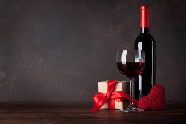 Sevgililer günü tebrik kartı ile kırmızı şarap şişesi, kara tahta önünde ahşap masa üzerinde kalp oyuncak ve hediye kutusu - Fotoğraf, Görsel