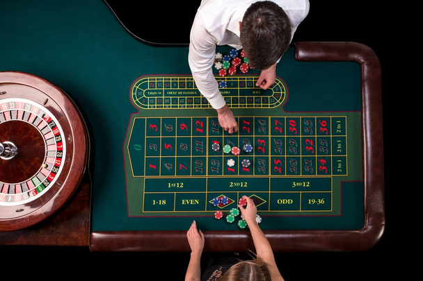 Krupié férfi és nő játszik rulettet a kaszinóban az asztalnál. Szemközti nézet egy zöld rulett asztal egy mérőszalag. - Fotó, kép