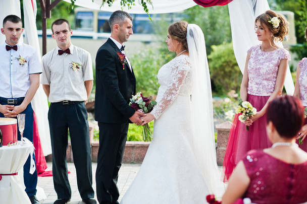 Bruidspaar geloften buiten onder de bloemenboog maken in fron - Foto, afbeelding