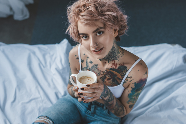 young tattooed girl with pink hair drinking coffee in bed at morning  - Photo, Image