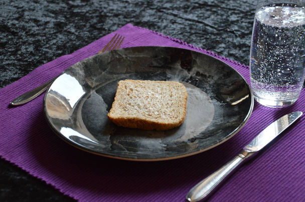 зменшена їжі у великий піст з шматочком хліба на тарілку і склянку води - Фото, зображення