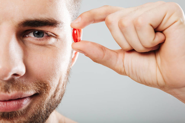 Close up portrait of a smiling man holding red capsule - Foto, imagen