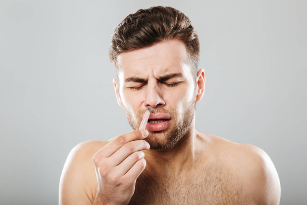 Man in pain removing nose hair with tweezers - Zdjęcie, obraz