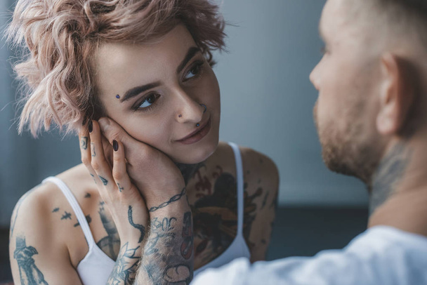 Нежный татуированный мужчина трогает лицо своей привлекательной девушки
 - Фото, изображение