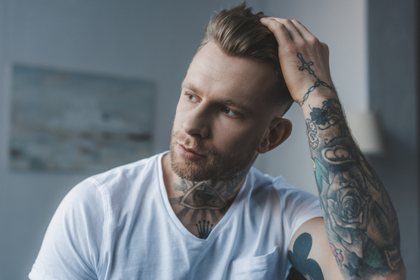 όμορφος μοντέρνος άνδρας τατουάζ αγγίζοντας τα μαλλιά του - Φωτογραφία, εικόνα