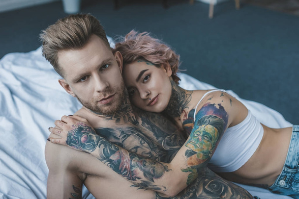 hombre y novia tatuados sin camisa abrazándose en la cama
 - Foto, Imagen