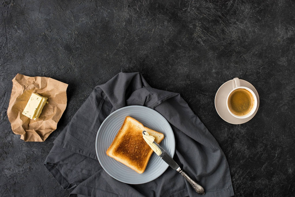 top view of toast, butter and cup of coffee for breakfast on dark surface - Photo, Image