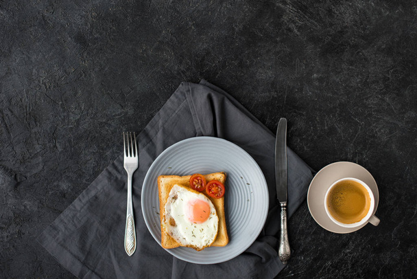 flat lay with cup of coffee and toast with fried egg and cherry tomatoes for breakfast on dark surface - Foto, Imagem