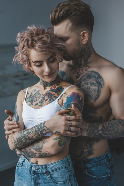 tender tattooed couple embracing in bedroom at home - Photo, Image