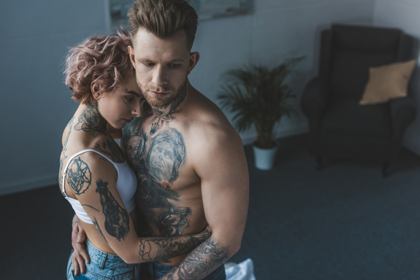 tender tattooed couple embracing in bedroom - Photo, Image