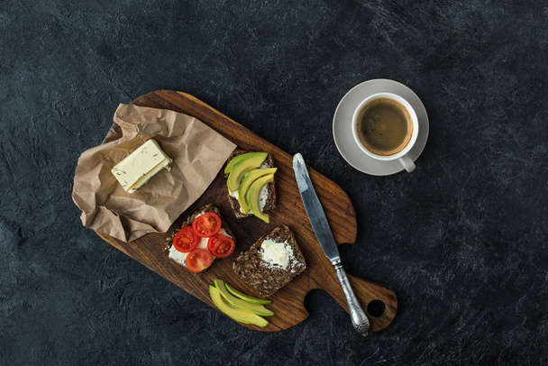 acostado plano con bocadillos para un desayuno saludable y una taza de café en la tabla de cortar de madera en la mesa oscura
 - Foto, Imagen