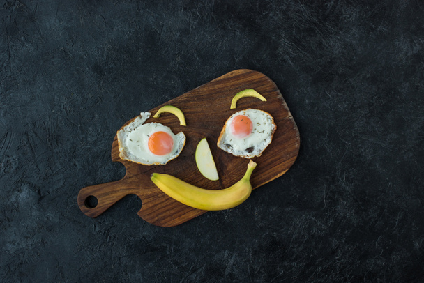 vista superior do rosto sorridente feito de alimentos para o café da manhã saudável na tábua de corte
 - Foto, Imagem