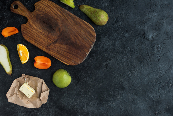 flat lay with fresh fruits, butter and empty cutting board on dark tabletop - Фото, изображение