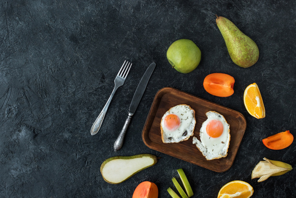 vlakke leggen met gezond ontbijt met gebakken eieren en vruchten op donkere tafelblad - Foto, afbeelding