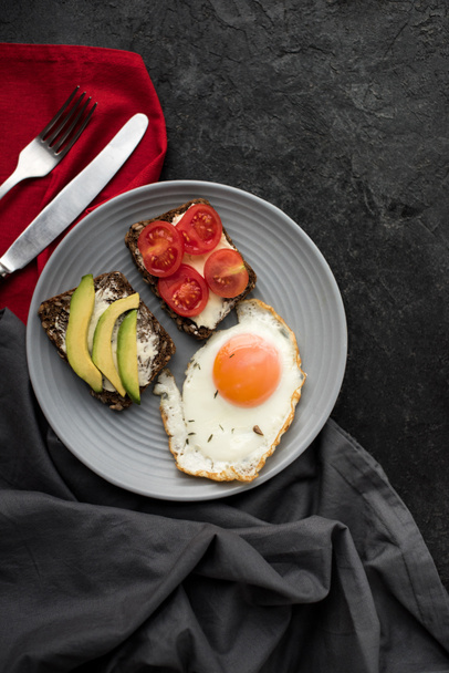 top view of fried egg and snacks for breakfast on plate on dark tabletop - Fotografie, Obrázek
