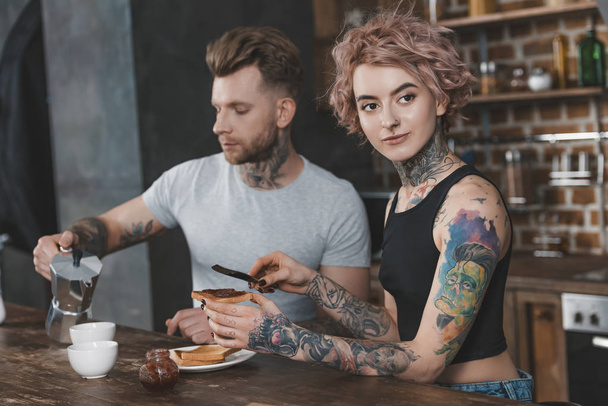 joven pareja tatuada comiendo tostadas y tomando café para el desayuno
  - Foto, Imagen