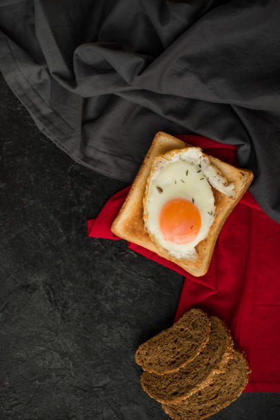ylhäältä näkymä paistettua munaa paahtoleipää ja viipaleita leipää tummalla pinnalla
 - Valokuva, kuva