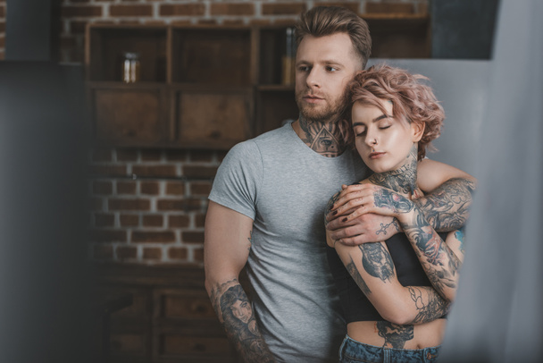 tender tattooed couple hugging in kitchen - Photo, Image