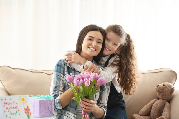 Young woman and her daughter with tulip bouquet indoors. Mother's day celebration - Фото, изображение