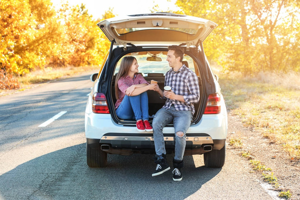 Beautiful young couple sitting with coffee in car trunk - Photo, Image