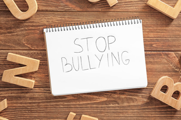 Notebook with text "Stop bullying" on wooden background, top view - Fotó, kép
