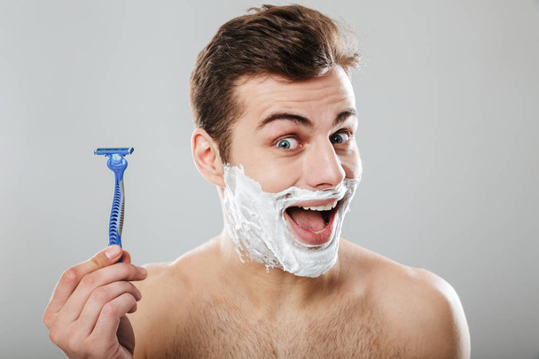Brunette happy guy 30s being undressed at bathroom with shaving  - Photo, Image