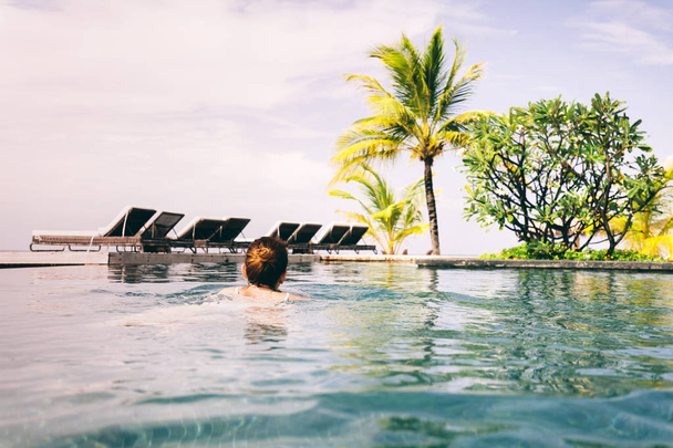 Frau schwimmt in einem Hotelpool mit Ruheplätzen in der Nähe. Tropenort. Sommeraktivitäten auf den Malediven - Foto, Bild