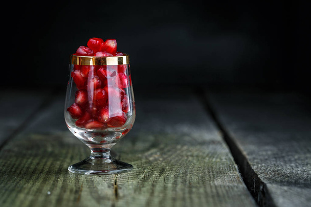 Ripe pomegranate seeds in a tiny glass on a vintage wooden background - Foto, Imagen