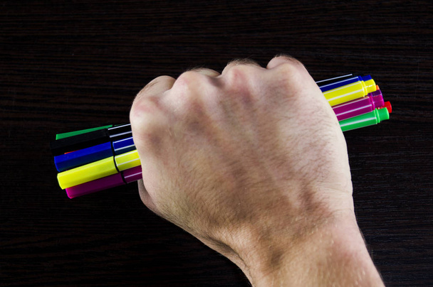Multicolored markers in a hand on a dark background table - Photo, image