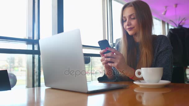 Mujer escribiendo mensajes de texto en un teléfono inteligente en un café. Mujer joven sentada en una mesa con un café usando un teléfono móvil. Con solapa de espacio de copia en blanco para su mensaje de texto publicitario o promocional
 - Metraje, vídeo
