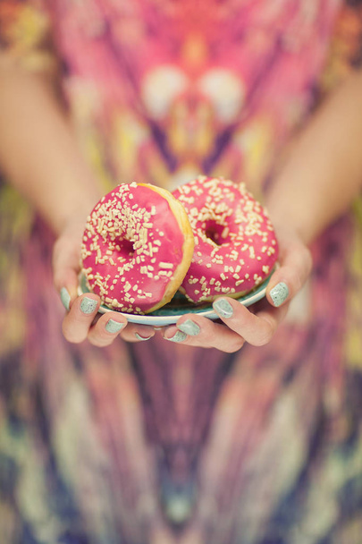 Woman hands with perfect nail polish holding a plate with pink donuts with pink pattern background - Photo, image