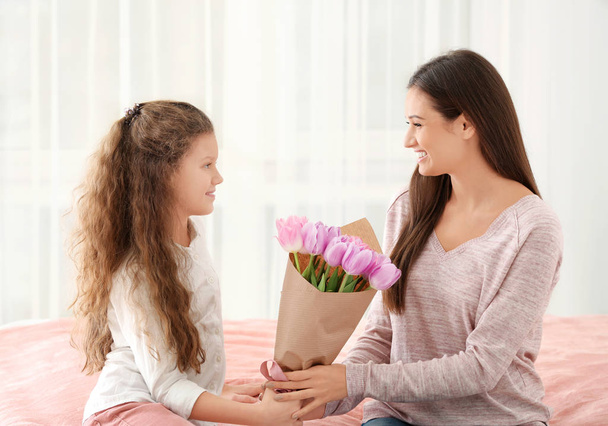 Cute little girl giving tulip bouquet to her mom indoors. Mother's day celebration - 写真・画像