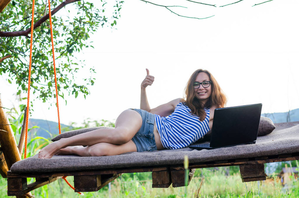 Усміхнена жінка працює на ноутбуці і показує знак ОК, на відкритому повітрі
. - Фото, зображення