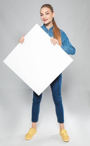 Young woman with blank advertising board on grey background - Foto, afbeelding