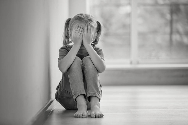 Θλιβερό κοριτσάκι που κάθεται στο πάτωμα στο εσωτερικό, ασπρόμαυρο εφέ - Φωτογραφία, εικόνα